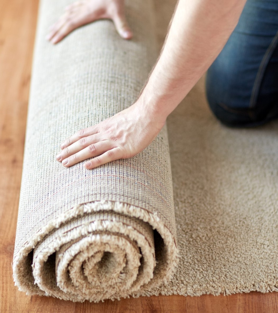repair, building and home concept – close up of male hands rolling carpet